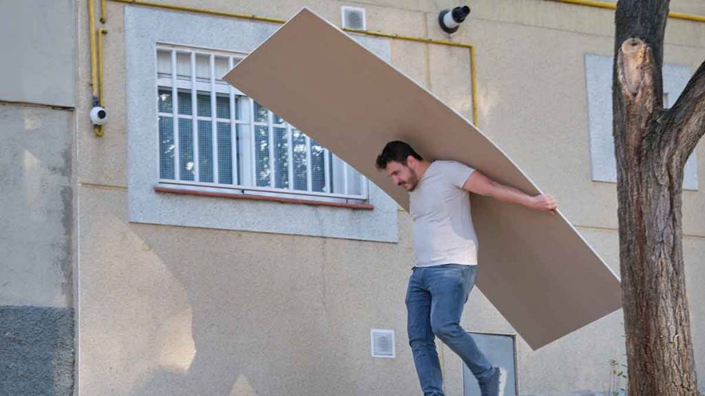 hombre cargando inadecuadamente una lámina de drywall